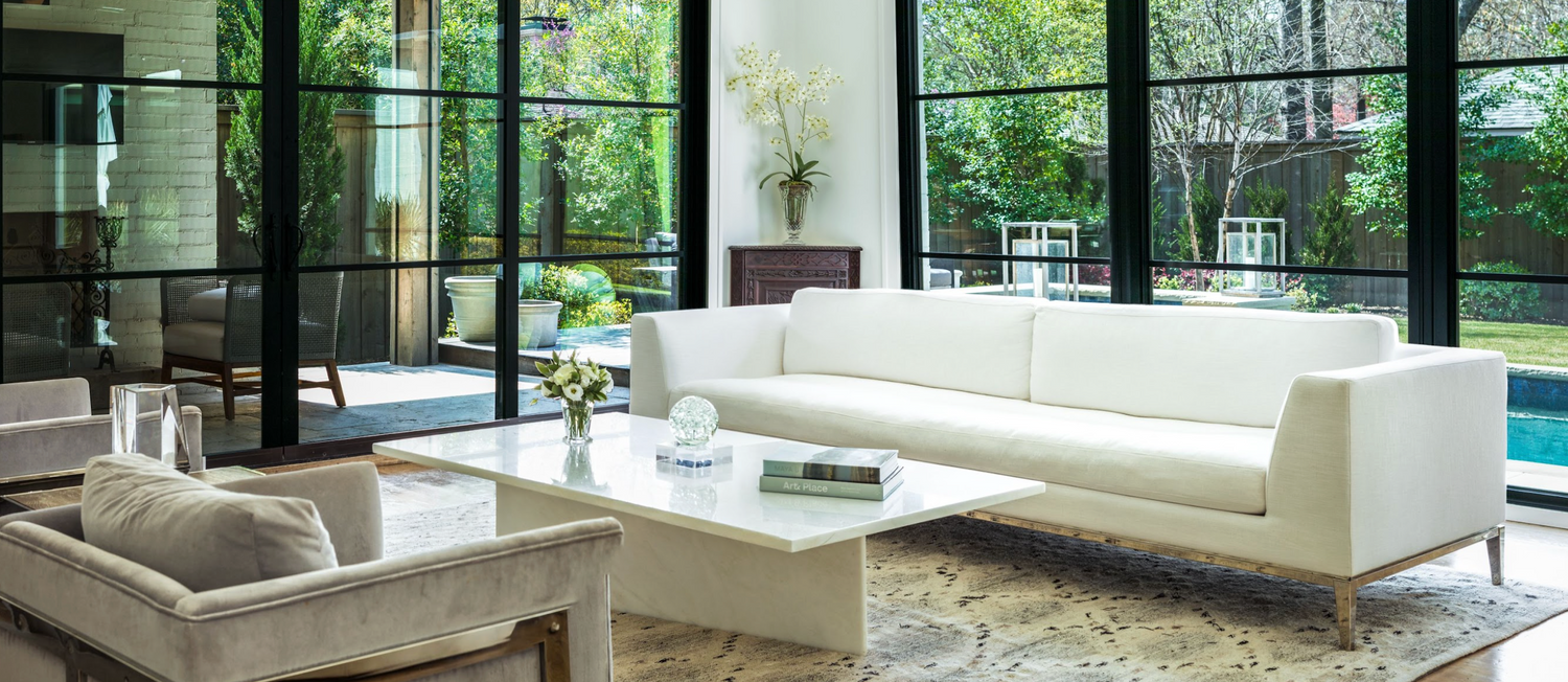 modern living room overlooking patio area with white couches and luxurious plants and decor.