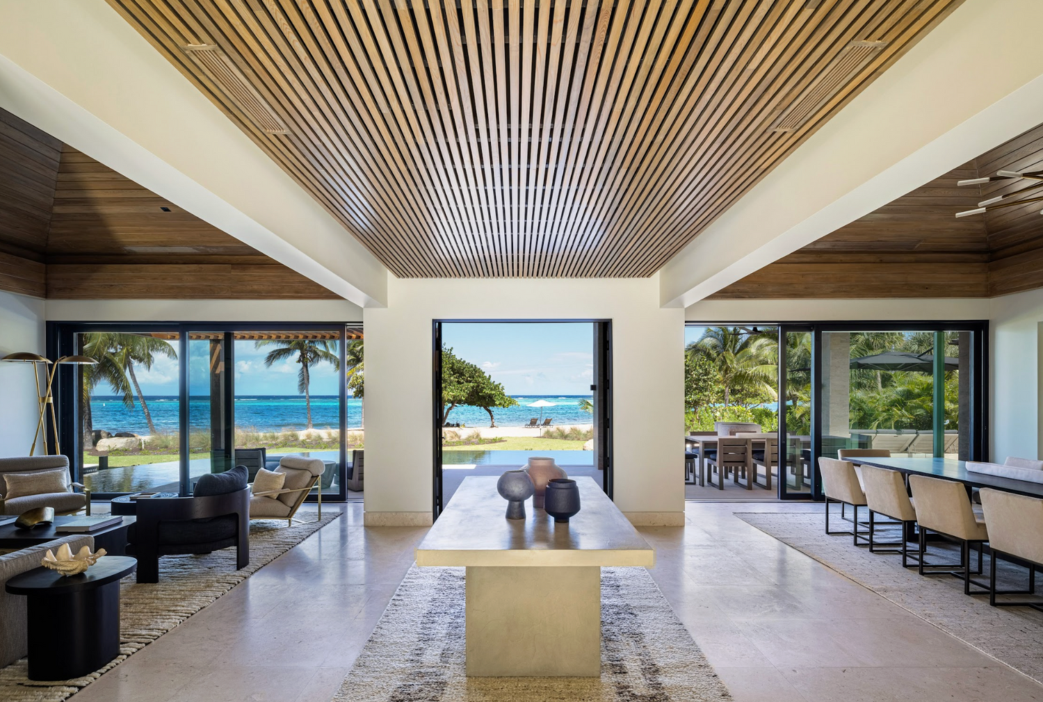 Modern interior with large windows overlooking a beach and palm trees.