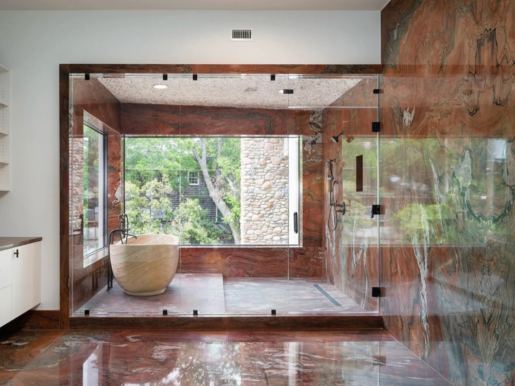 Modern bathroom with glass shower enclosure and bathtub, featuring a view of trees outside.