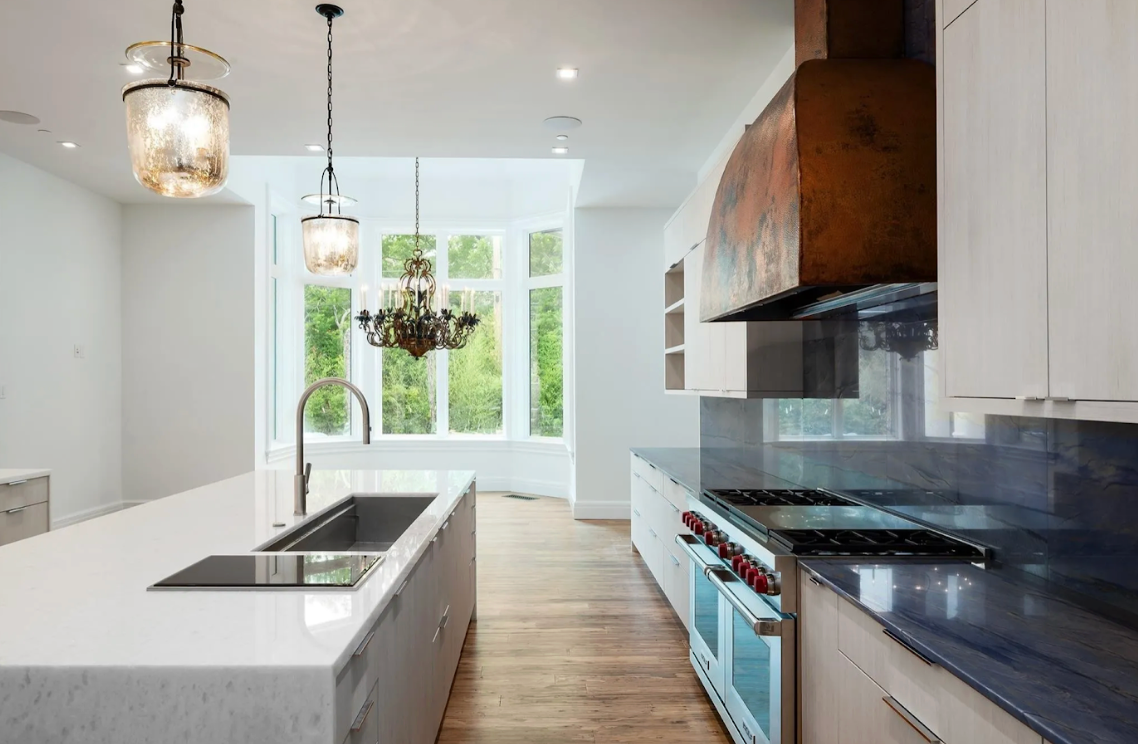 Modern kitchen with white island, stainless steel appliances, and large windows.