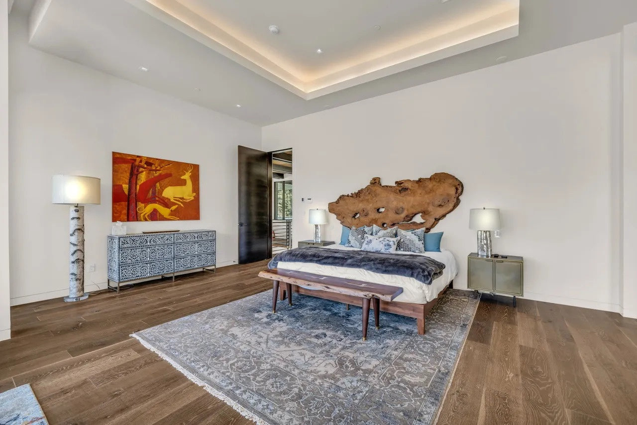 Modern bedroom with wooden headboard, bench, and abstract art on wall.