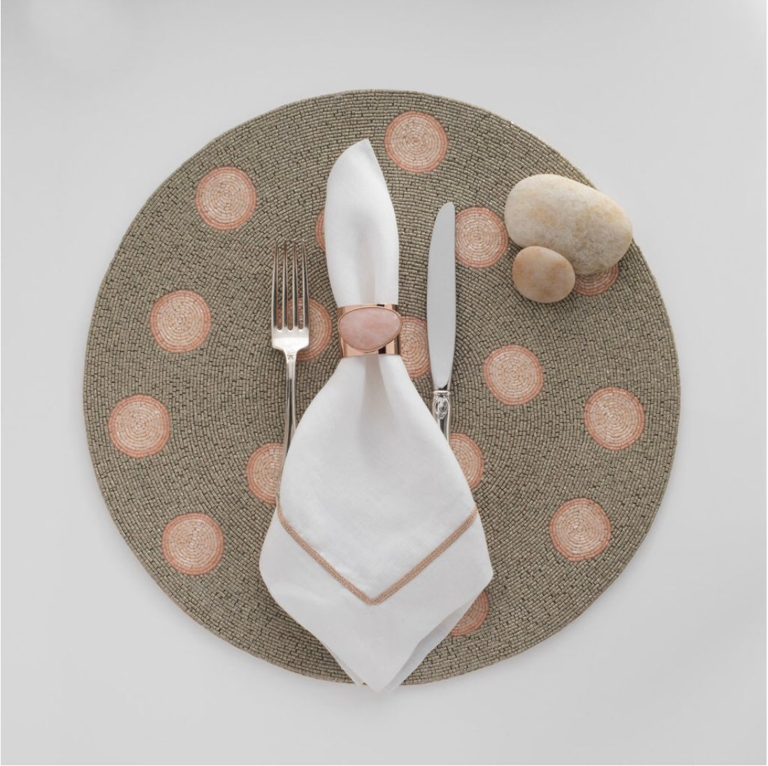 Dark beige placemat with pink spots and utensil & napkin setup with pink stone napkin holder.