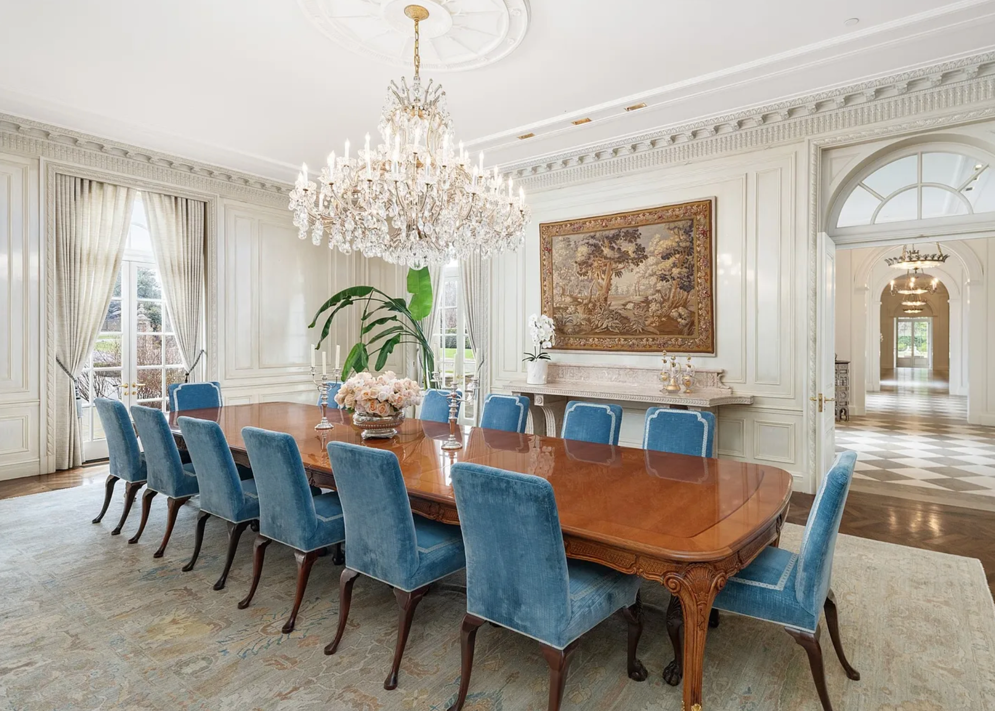 Long dining table with blue felt chairs and crystal chandelier hanging above.