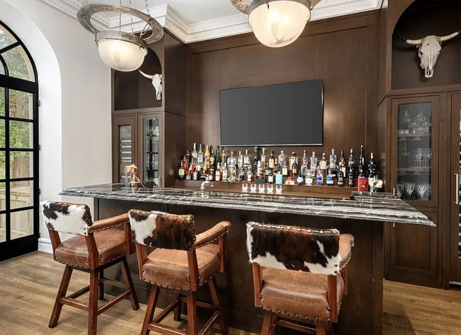 Rustic home bar with cow printed bar stools and tv in background.