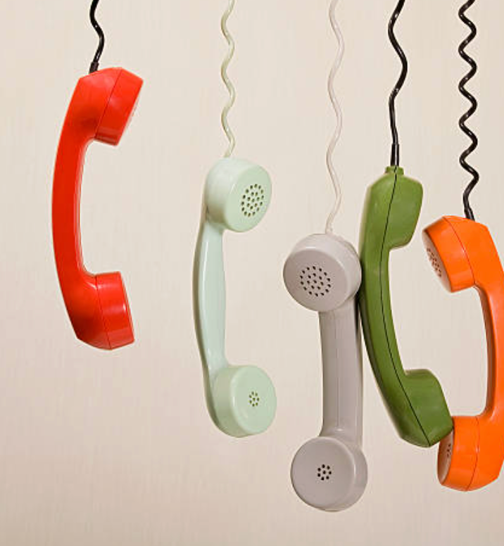 5 old telephones hang by the cord 