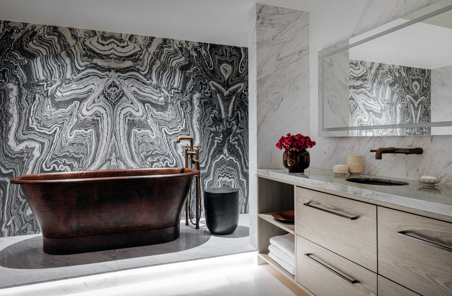 Modern bathroom with a freestanding copper bathtub, marble wall, and vanity area.