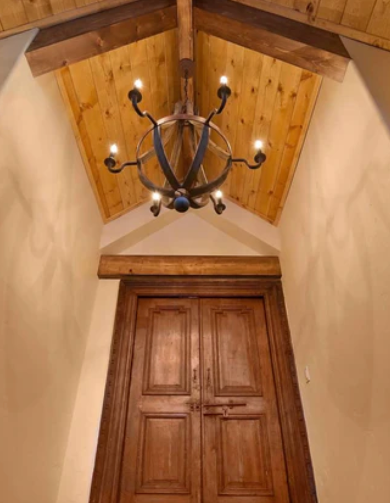 Wooden chandelier hanging from a vaulted ceiling with wooden doors below.