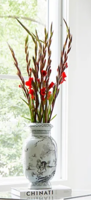 Decorative vase with red flowers on a white surface near a window