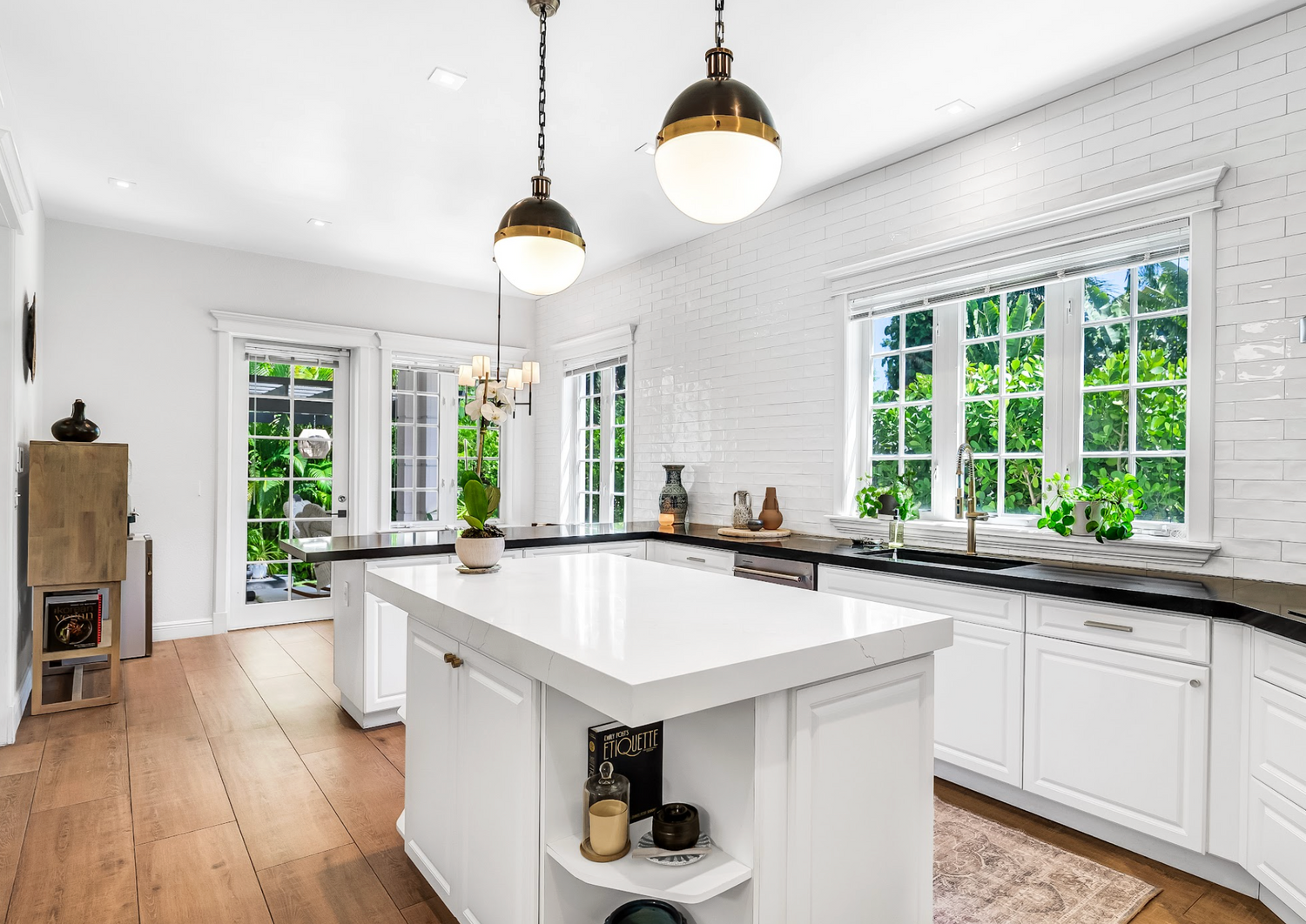 Modern kitchen with white island, black countertops, and large windows.