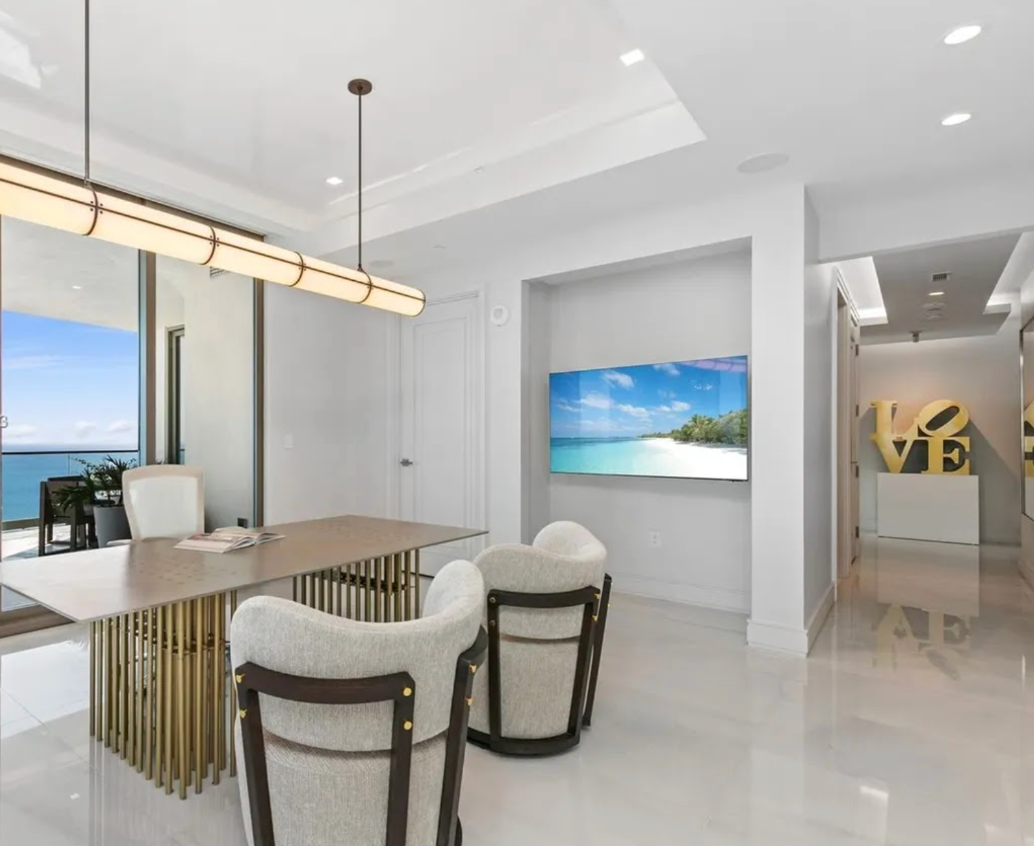 Modern interior with a dining table and chairs, large screen displaying a beach scene, and abstract art on the wall.