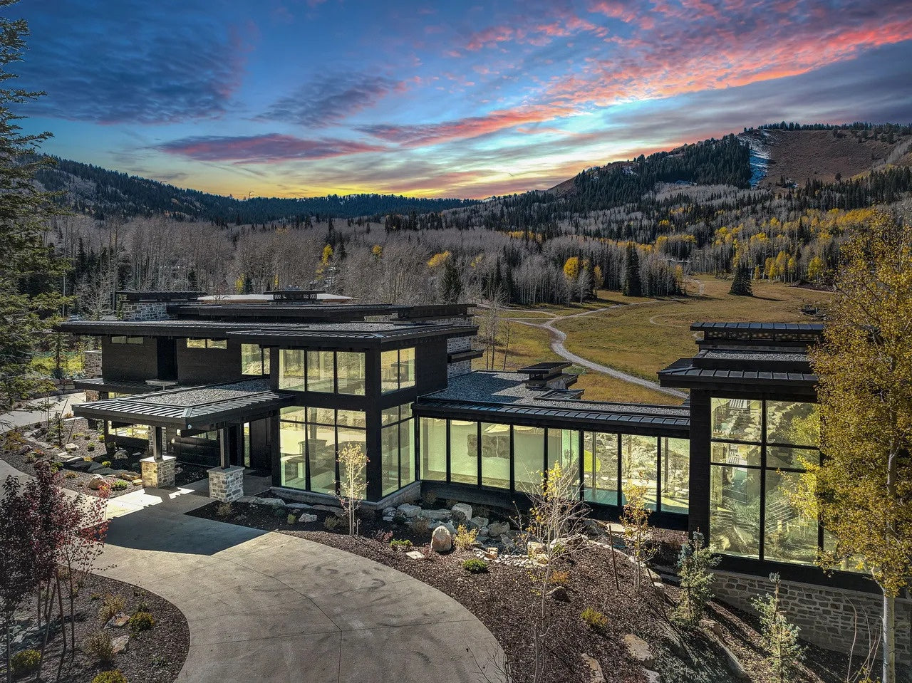 Modern house with large glass windows in a mountainous area during sunset.